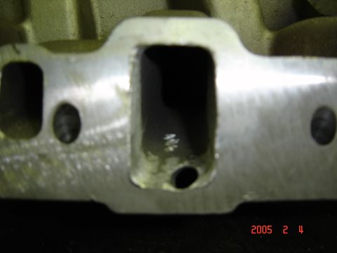 1990 Ford Bronco - Extreme close-up of the intake-port face of a bare cast-iron cylinder head, showing a freshly machined mating surface and rectangular ports…