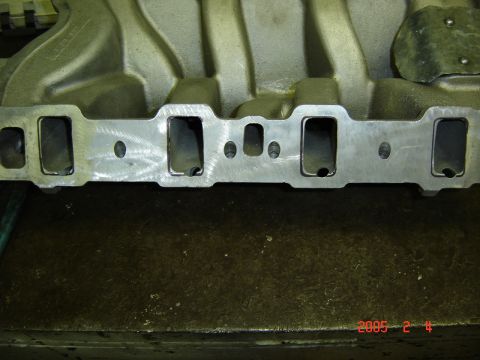 1990 Ford Bronco - Close-up of the cylinder-head mating flange on an aluminum V8 intake manifold sitting on a workbench, showing rectangular intake ports, coo…