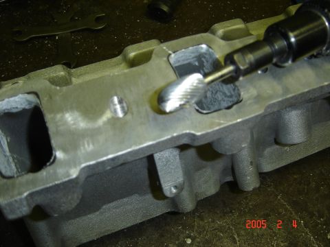 1990 Ford Bronco - Close-up of a bare aluminum cylinder head on a workbench being port-matched with a die grinder and carbide burr at the rectangular intake p…