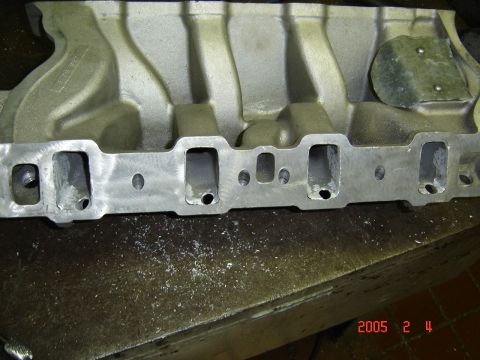 1990 Ford Bronco - Aluminum intake manifold lying on a workbench with its cylinder-head mating flange facing the camera, showing four rectangular intake ports…
