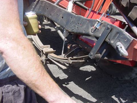 1985 Ford Bronco - Close-up view of a vehicle's leaf spring suspension system, with a person's arm and hand holding a beverage can visible.