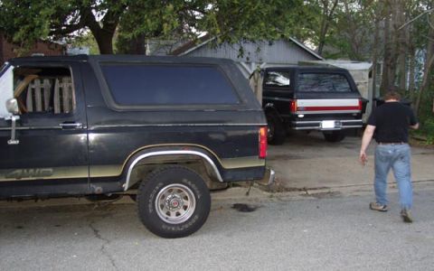 1988 Ford Bronco - Two Ford Broncos are parked in a driveway. One is in the foreground, and another is behind it. A man walks away from the vehicles.