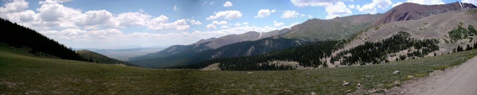 Wide mountain valley with green grass in the foreground and trees on the slopes