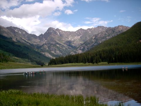 1986 Ford Bronco - A scenic view of a lake surrounded by mountains and pine forests, with people in boats on the water.