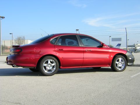 1997 Ford Taurus - This red sedan is parked outside on a clear day with a fence and buildings in the background.