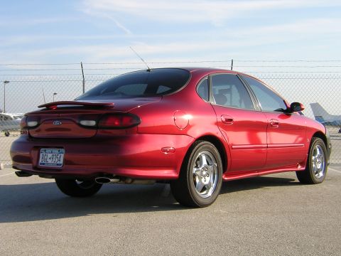 1997 Ford Taurus - A red sedan with a spoiler is parked outdoors under a clear sky.