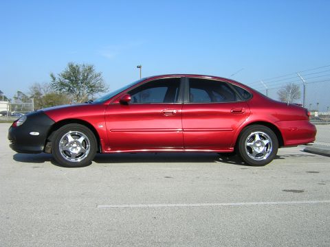 1997 Ford Taurus - Side view of a red sedan, identified as a 2000 model year based on its body style, equipped with a black car bra.