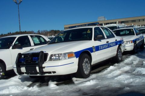 2001 Ford Crown Victoria - Multiple 2001 Ford Crown Victoria police cars are parked in a snowy lot under a clear blue sky.