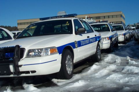 2001 Ford Crown Victoria - A line of white transit police vehicles with blue stripes and lights are parked in a snowy lot.