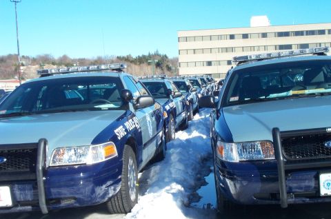 2001 Ford Crown Victoria - Multiple Ford Crown Victoria police cruisers lined up in a snowy lot under a clear sky.