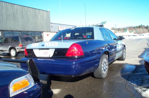 2001 Ford Crown Victoria - A blue and grey police car is parked in a lot with snow on the ground. Another police car is partially visible in the foreground.