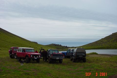 1993 Ford Bronco - A group of off-road vehicles are gathered in a scenic landscape with a lake and rolling hills.