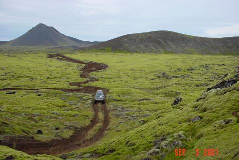 1993 Ford Bronco - An SUV navigates a muddy track across a vast, green, and rocky landscape under a cloudy sky.