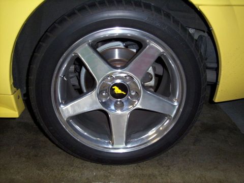 2002 Ford Mustang - Close-up of a yellow Ford Mustang wheel with a chrome rim and a running horse emblem.