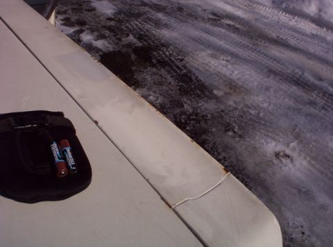1991 Ford LTD Crown Victoria - A close-up of a car's hood shows a pouch with batteries, set against a backdrop of snowy ground with tire tracks.
