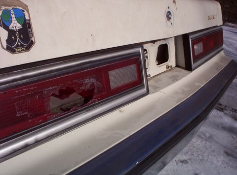 1991 Ford LTD Crown Victoria - The rear of a car shows a damaged taillight and a space shuttle sticker.