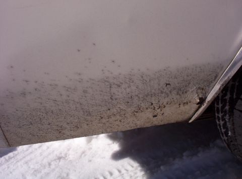 1991 Ford LTD Crown Victoria - The lower section of a vehicle's body is covered in mud and dirt, with snow visible below.