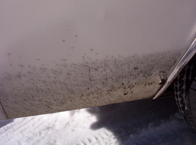 Close-up of a dirty lower car panel with snow on the ground