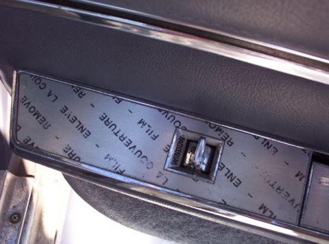 1991 Ford LTD Crown Victoria - Close-up of a car's interior door panel, showing a window switch still covered by its original protective film.