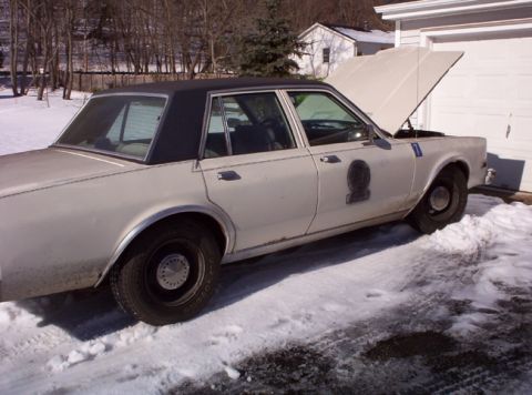 1991 Ford LTD Crown Victoria - This 1979 Dodge St. Regis police car is parked outside in the snow with its hood up.
