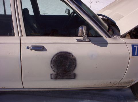1991 Ford LTD Crown Victoria - A white 1991 Ford Crown Victoria is shown from the side, a circular emblem and a racing number on its fender.