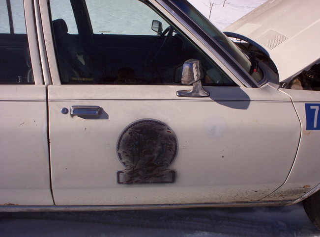 Side view of a white 1991 Ford Crown Victoria with a circular emblem on the door and a blue number 7 on the fender