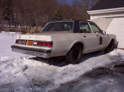 1991 Ford LTD Crown Victoria - A white sedan with a black vinyl roof sits in the snow, its hood open, parked next to a garage.
