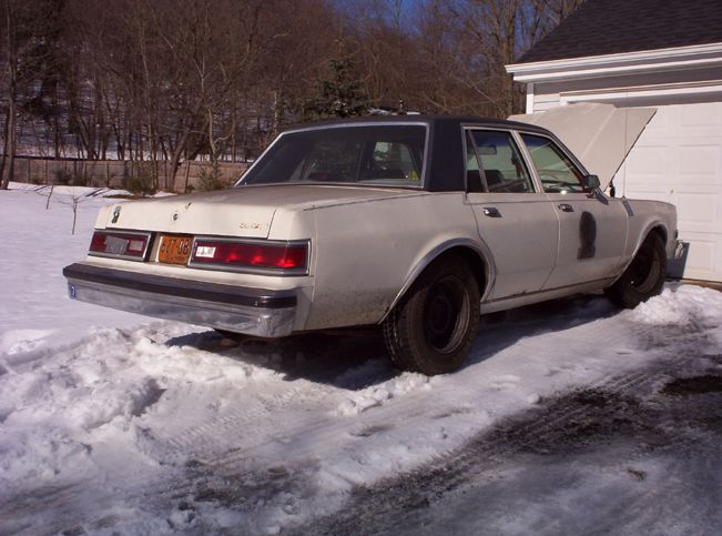 White sedan with black roof parked in snow, rear view. License plate reads 687-06