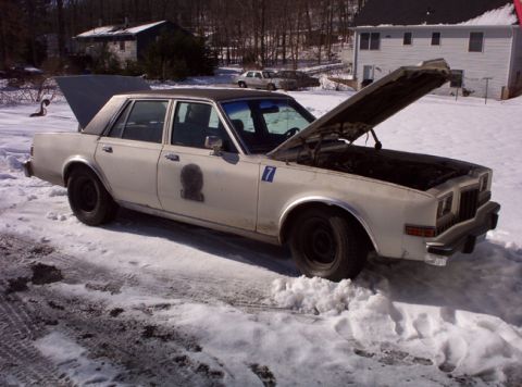 1991 Ford LTD Crown Victoria - This older model sedan, possibly a former police car, sits in the snow with its hood and trunk open.