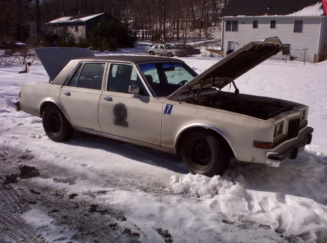 White sedan with hood and trunk open, parked in snow. Has a shield emblem and number 7 on the door