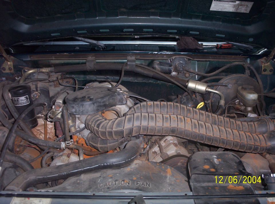 Engine bay with black air intake duct and 'CAUTION FAN' shroud, dusty and rusty.