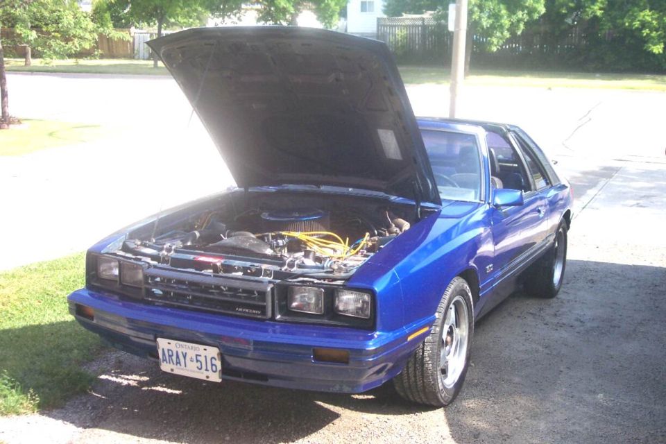Blue 1980s coupe with hood up showing engine bay, Ontario ARAY-516 plate