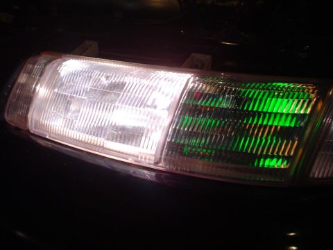 1993 Ford Taurus - Close-up of a 1993 Ford Taurus headlight assembly, showing the clear main beam and the green turn signal.