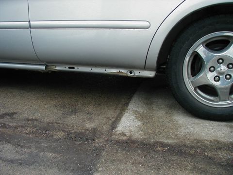 1997 Ford Taurus - Close-up of a silver car's damaged lower side panel and wheel.