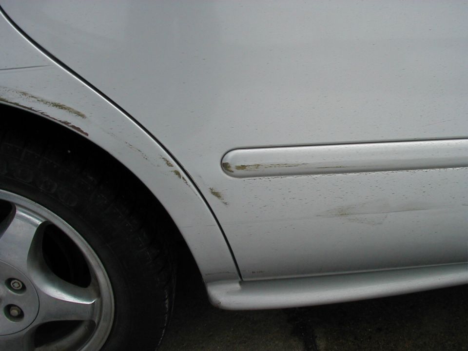 Silver 1997 Ford Taurus rear quarter panel and wheel with scuffs and dirt