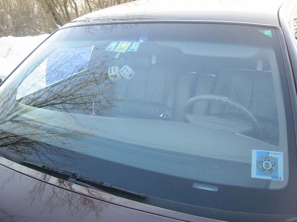Car interior showing dashboard, steering wheel, and seats through the windshield. Dice hanging from rearview mirror