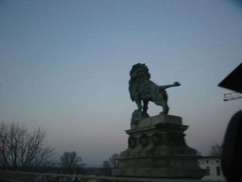 1992 Ford Crown Victoria - A bronze lion statue stands atop a stone pedestal under a fading sky.