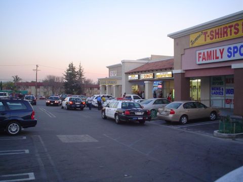 1993 Ford Taurus - Police activity observed in a parking lot outside a strip mall with businesses like 'Famous T-Shirts' and 'Family Sport'.