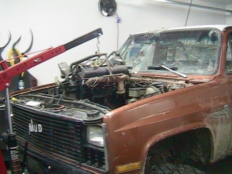 1981 Chevrolet C/K Pickup - A truck's engine is being removed using an engine hoist in a garage setting.