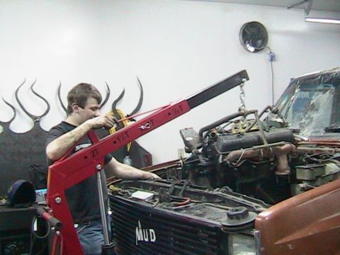 1981 Chevrolet C/K Pickup - A person uses an engine hoist to remove the engine from a pickup truck in a garage.
