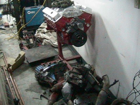 1981 Chevrolet C/K Pickup - Engine on a stand in a workshop setting, with other engine parts on the floor.
