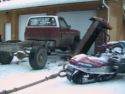 1981 Chevrolet C/K Pickup - A 1981 Chevrolet C/K Pickup chassis sits in the snow, tethered to a Polaris snowmobile.