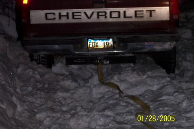 Maroon Chevrolet pickup stuck in deep snow at night with a recovery strap on the hitch