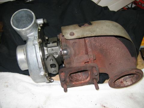 1985 Ford LTD Crown Victoria - A turbocharger lying on a white towel over black fabric, showing a bare aluminum compressor housing with inlet neck on the left and a rust-…