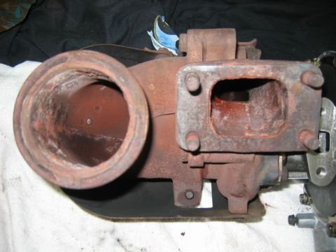 1985 Ford LTD Crown Victoria - A heavily rusted cast-iron turbocharger turbine housing rests on a white shop towel, showing its large round exhaust outlet, four-bolt rect…