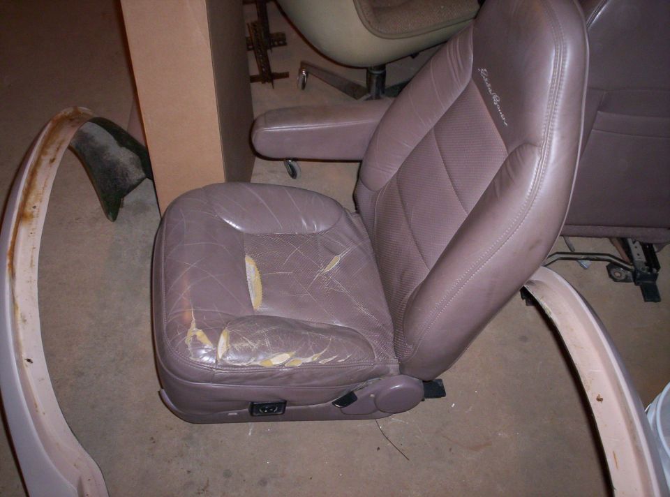 Worn brown leather car seat with tears on the cushion and armrest. Other car parts are visible in the background