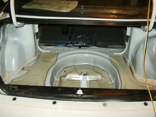 Stripped trunk of a white sedan showing the bare empty spare-tire well