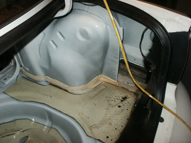 Stripped car interior with bare gray floor pan, rear wheel arch and cracked tan sound deadening