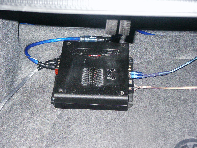 Black Kicker amplifier in trunk with blue wiring and copper ground cable