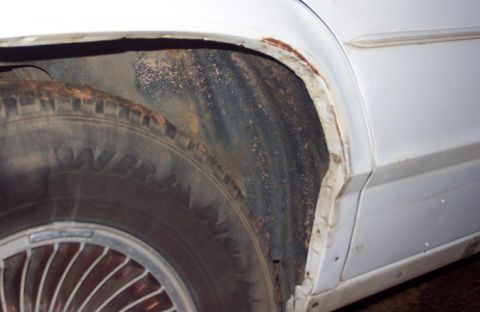 1985 Ford LTD Crown Victoria - Rust is visible on the fender and wheel well of a white car, indicating poor condition.